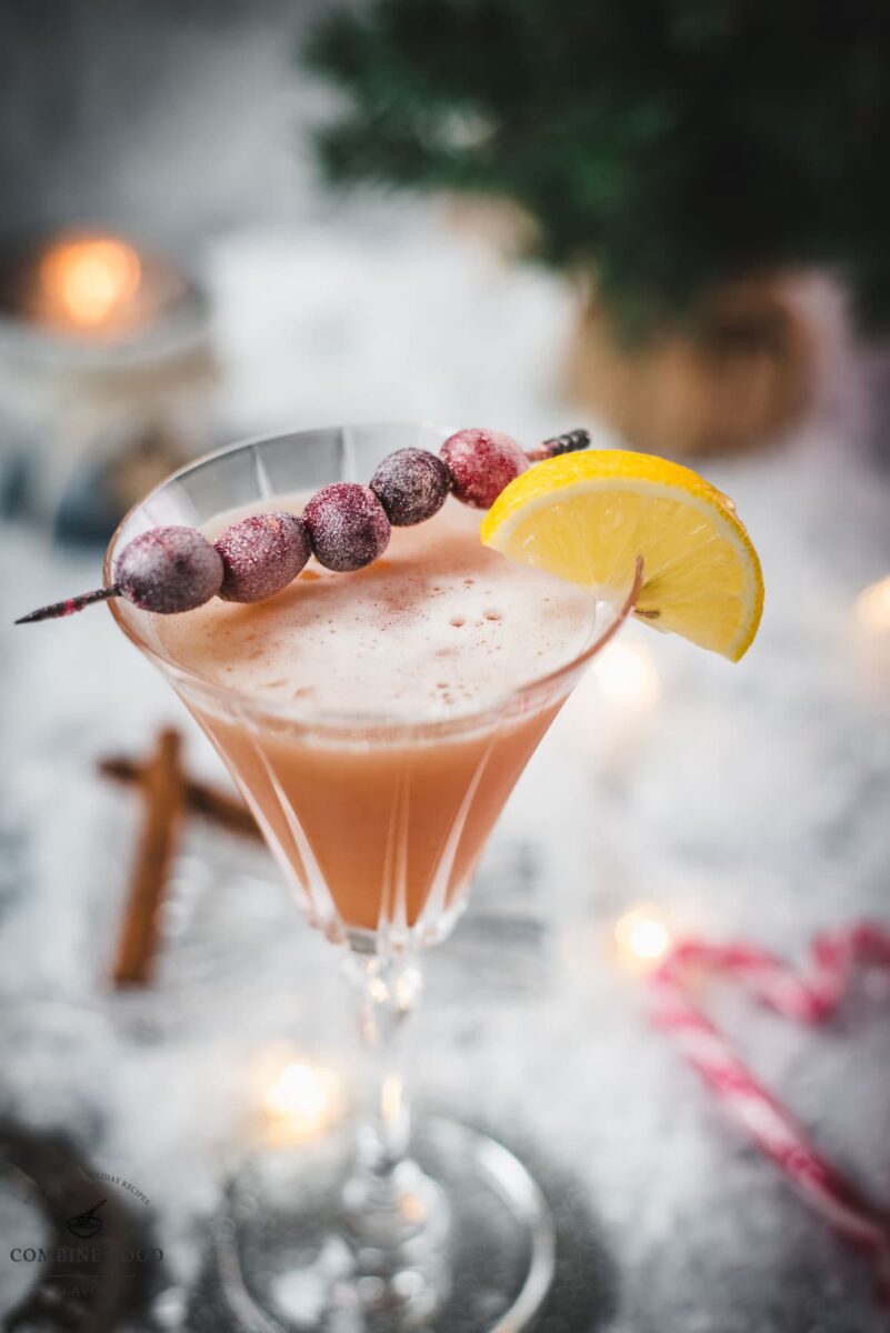 Festive cranberry cinnamon whiskey sour in gorgeous glass, placed on ice ground next to cinnamon sticks and candy canes.