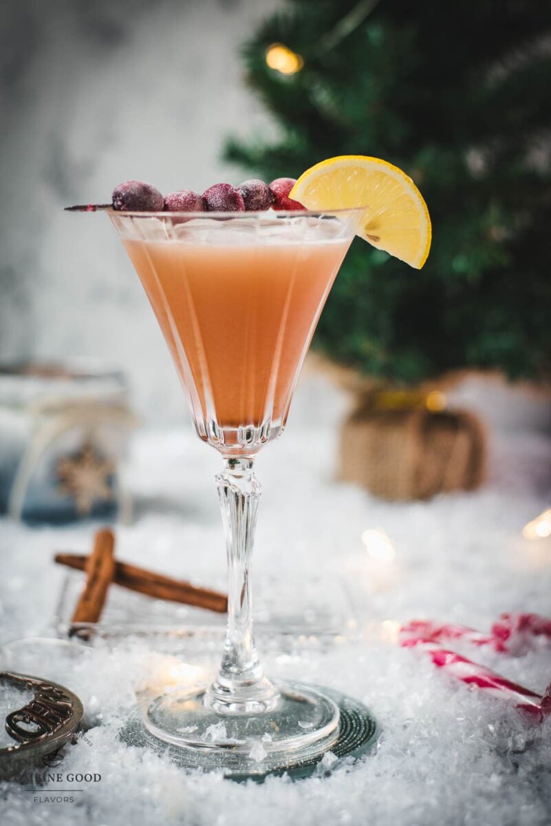 Festive cranberry cinnamon whiskey sour in gorgeous glass, placed on ice ground next to cinnamon sticks and candy canes.