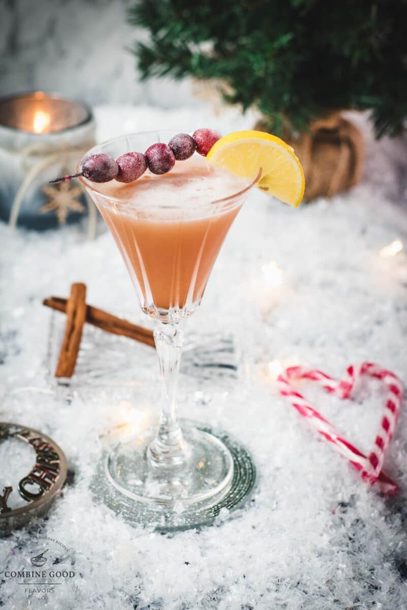 Festive cranberry cinnamon whiskey sour in gorgeous glass, placed on ice ground next to cinnamon sticks and candy canes.