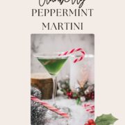 Festive cranberry peppermint martini in sugar rimmed martini glass. Garnished with a candy cane, placed on snowy ground.