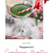 Festive cranberry peppermint martini in sugar rimmed martini glass. Garnished with a candy cane, placed on snowy ground.