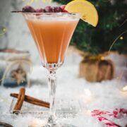 Festive cranberry cinnamon whiskey sour in gorgeous glass, placed on ice ground next to cinnamon sticks and candy canes.