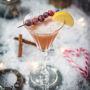 Festive cranberry cinnamon whiskey sour in gorgeous glass, placed on ice ground next to cinnamon sticks and candy canes.