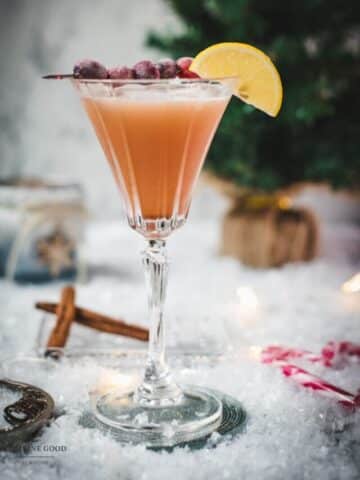 Festive cranberry cinnamon whiskey sour in gorgeous glass, placed on ice ground next to cinnamon sticks and candy canes.