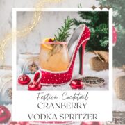 Festive vodka cranberry spritzer, garnished with rosemary twig, orange slice, and cranberries, served in a glass that is placed in a christmassy red high heel.