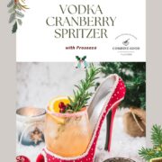 Festive vodka cranberry spritzer, garnished with rosemary twig, orange slice, and cranberries, served in a glass that is placed in a christmassy red high heel.