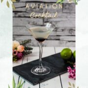 Elegant cocktail glass filled with a delicious aviation cocktail and garnished with a maraschino cherry. Placed on a black slate plate.