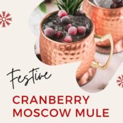 Two copper mugs filled with a delicious cranberry Moscow mule, placed on mirrored coaster and garnished with rosemary twigs and frozen cranberries.