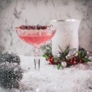 Gorgeous pink cranberry maraschino sour garnished with iced cranberries on a cocktail skewer.