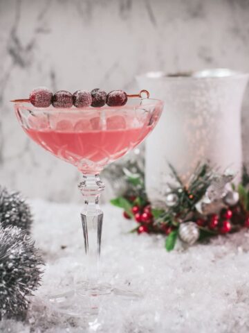 Gorgeous pink cranberry maraschino sour garnished with iced cranberries on a cocktail skewer.