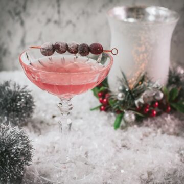 Gorgeous pink cranberry maraschino sour garnished with iced cranberries on a cocktail skewer.