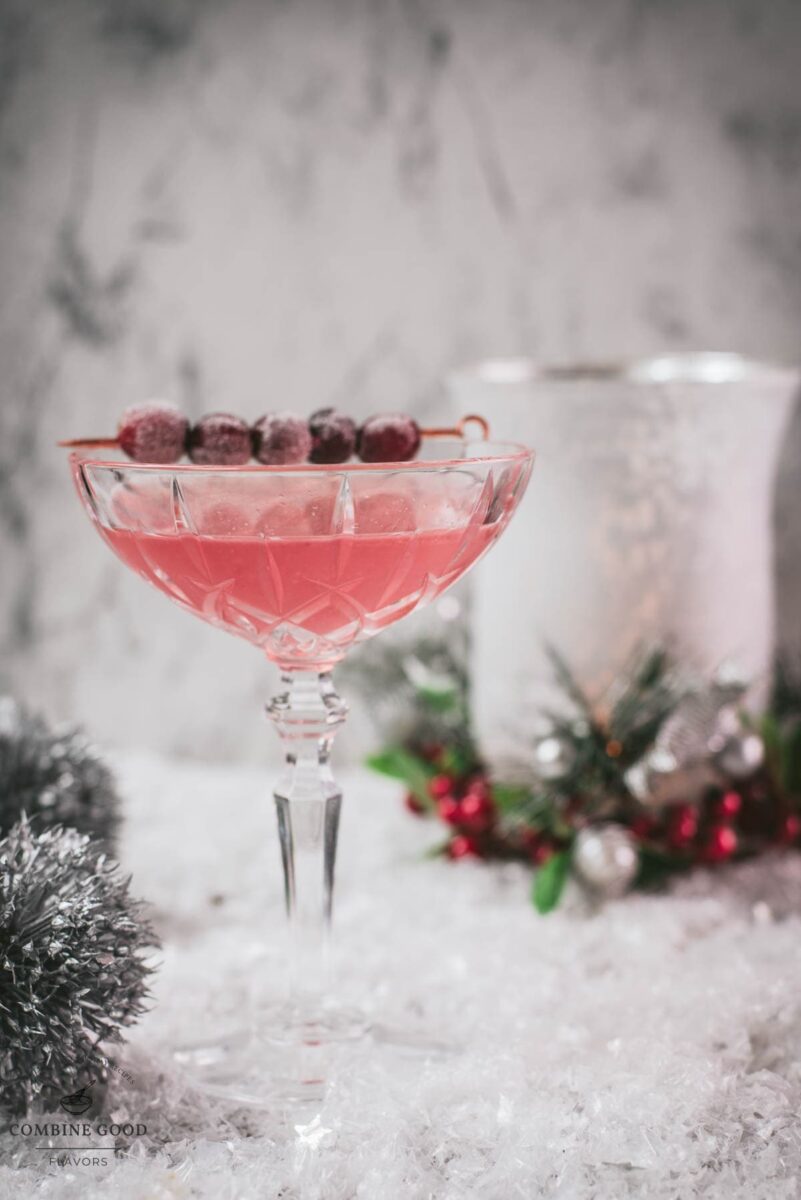 Gorgeous pink cranberry maraschino sour garnished with iced cranberries on a cocktail skewer.