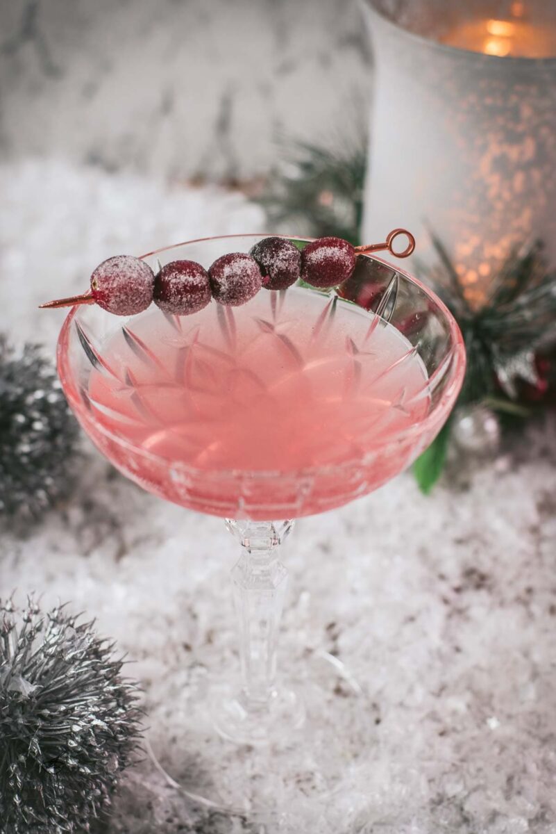 Gorgeous pink cranberry maraschino sour garnished with iced cranberries on a cocktail skewer.