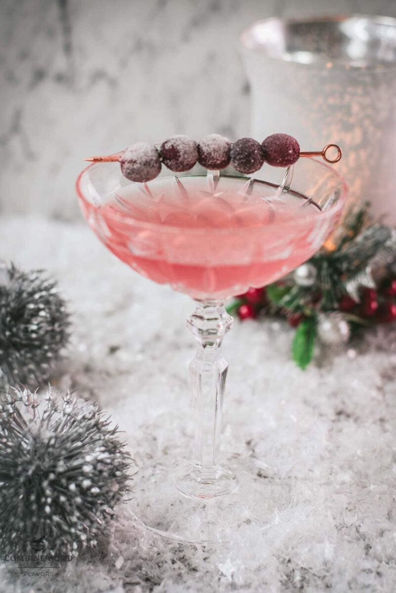 Gorgeous pink cranberry maraschino sour garnished with iced cranberries on a cocktail skewer.