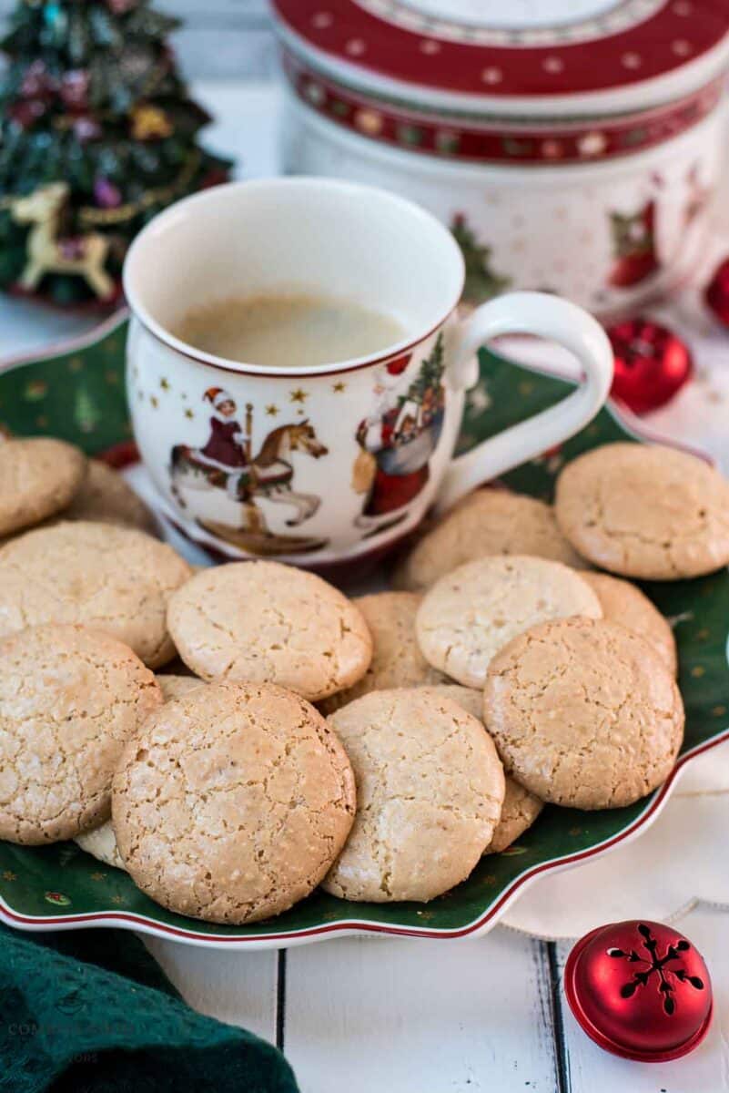 Delicious hazelnut meringue cookies placed on green christmassy plate, next to a coffee mug.