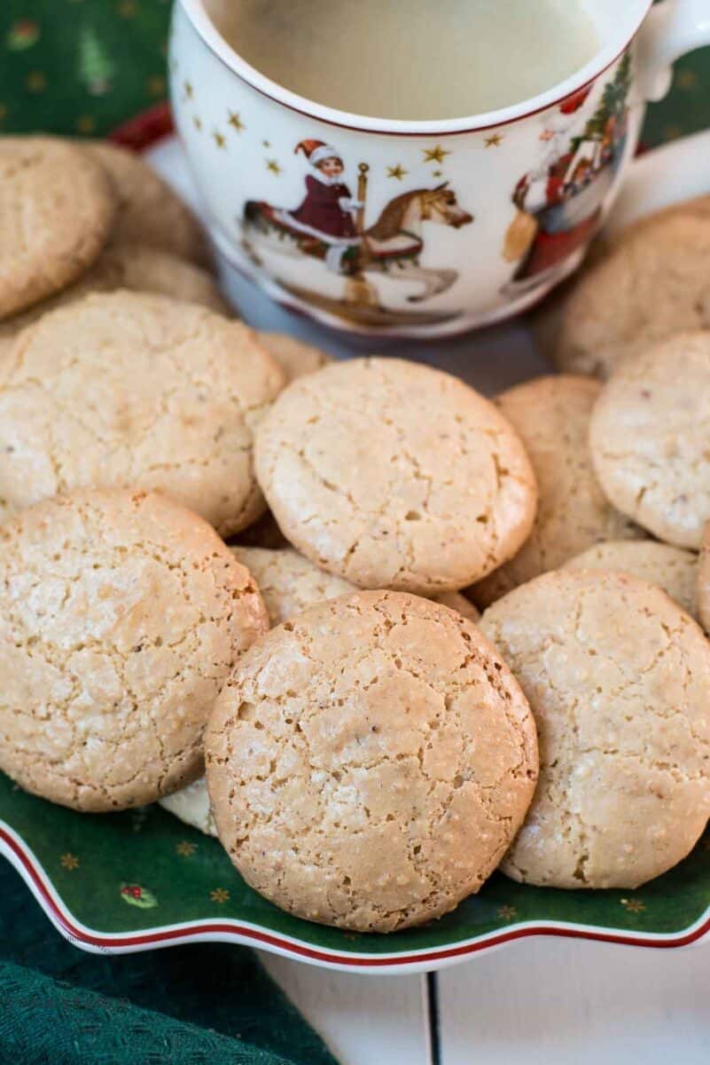 Delicious hazelnut meringue cookies placed on green christmassy plate, next to a coffee mug.