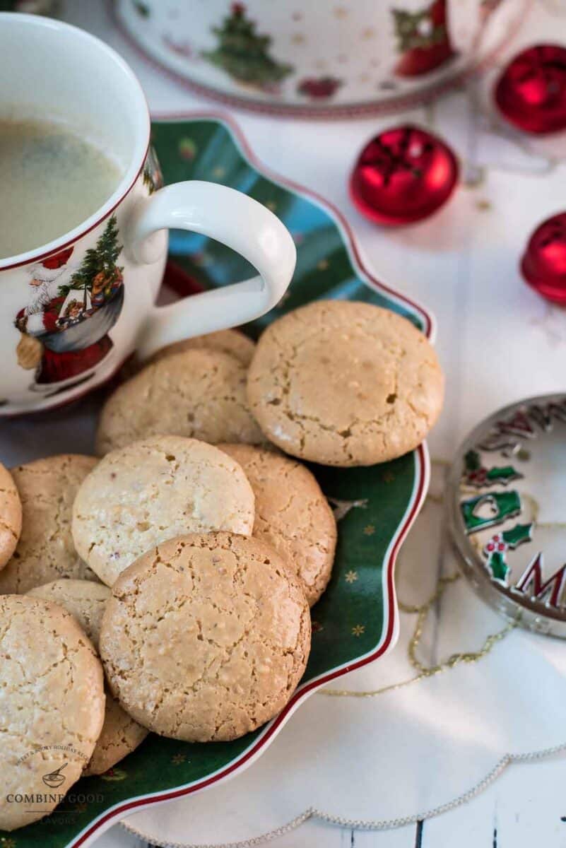 Delicious hazelnut meringue cookies placed on green christmassy plate, next to a coffee mug.