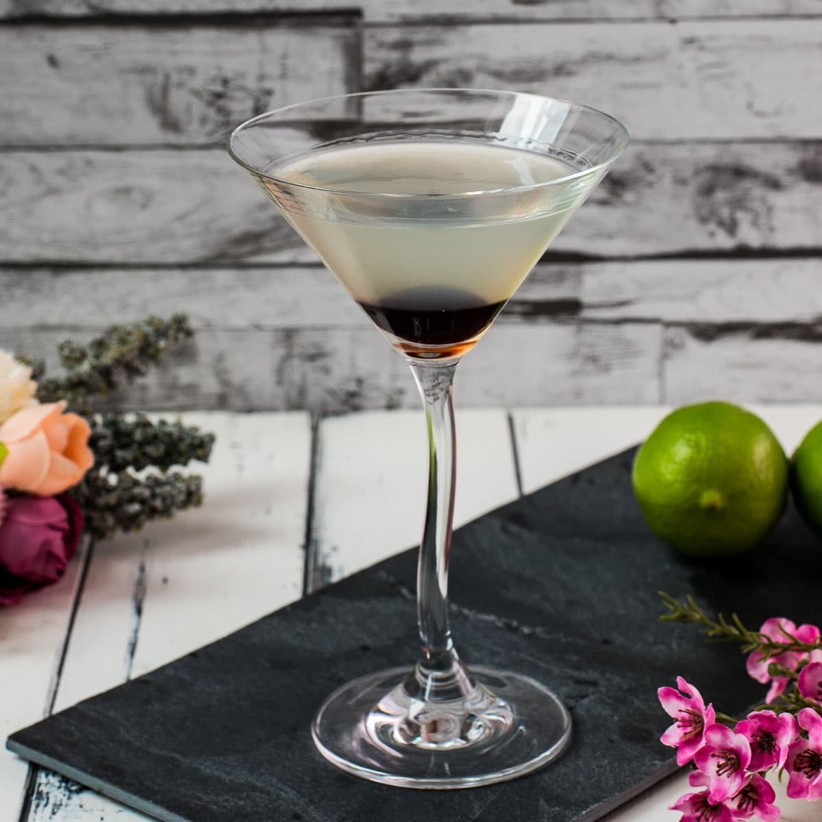 Elegant cocktail glass filled with a delicious aviation cocktail and garnished with a maraschino cherry. Placed on a black slate plate.