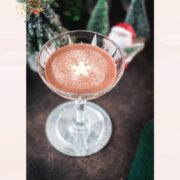 Festive chocolate martini with a white chocolate snowflake garnish, placed on mirrored coaster next to a Santa clause figurine.