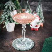 Festive chocolate martini with a white chocolate snowflake garnish, placed on mirrored coaster next to a Santa clause figurine.