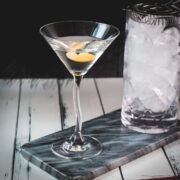 Elegant cocktail glass, placed on marbled plate, and garnished with a lemon zest.