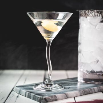 Elegant cocktail glass, placed on marbled plate, and garnished with a lemon zest.