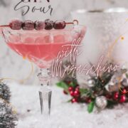 Gorgeous pink cranberry maraschino sour garnished with iced cranberries on a cocktail skewer.