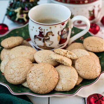 Delicious hazelnut meringue cookies placed on green christmassy plate, next to a coffee mug.