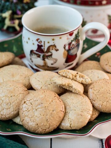 Delicious hazelnut meringue cookies placed on green christmassy plate, next to a coffee mug.