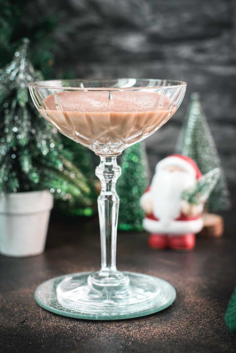 Festive chocolate martini with a white chocolate snowflake garnish, placed on mirrored coaster next to a Santa clause figurine.