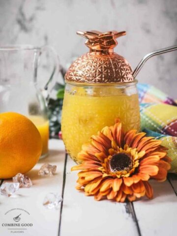 Classic screwdriver cocktail, served in pineapple shaped cocktail glass, placed next to an orange flower.