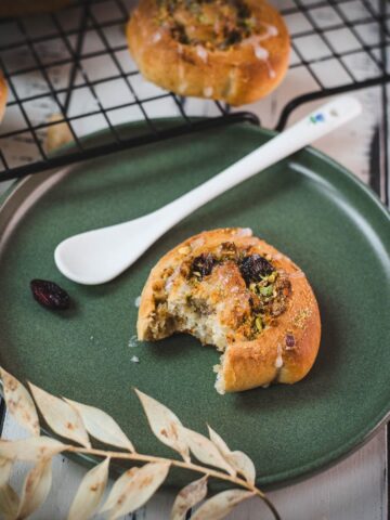 A delicious, half-eaten mini pistachio sweet roll on a green plate.