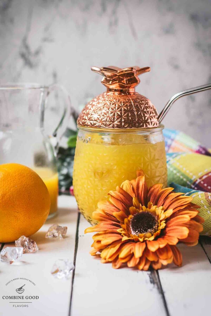 Classic screwdriver cocktail, served in pineapple shaped cocktail glass, placed next to an orange flower.