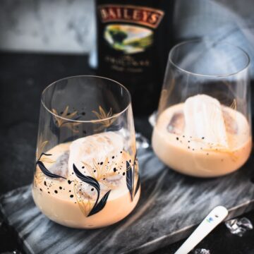 Cute tumbler glasses filled with delicious Baileys Irish Cream on the rocks. Placed on marbled plate.