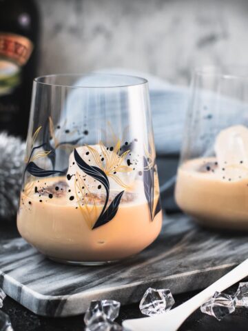 Cute tumbler glasses filled with delicious Baileys Irish Cream on the rocks. Placed on marbled plate.