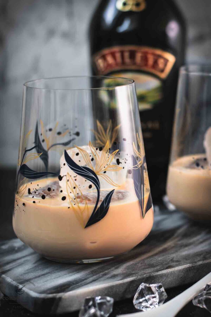 Cute tumbler glasses filled with delicious Baileys Irish Cream on the rocks. Placed on marbled plate.