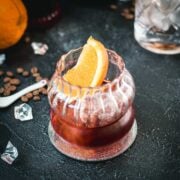 Gorgeous rocks glass, filled with a delicious cold brew negroni, garnished with an orange slice, and placed on a mirrored coaster.