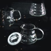 Gorgeous glass carafes, placed on dark ground, next to scattered coffee beans.