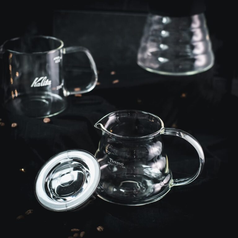 Gorgeous glass carafes, placed on dark ground, next to scattered coffee beans.