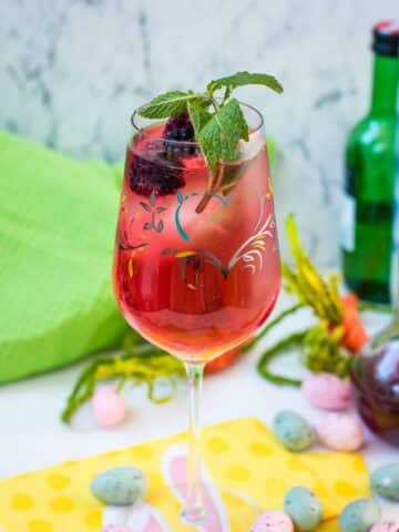 Cute white wine glass, filled with a delicious Blackberry Raspberry Easter Spritz. Garnished with blackberries and mint spring.