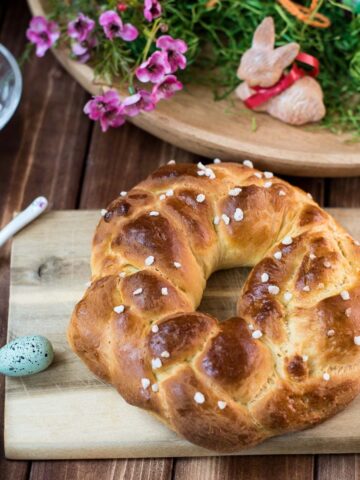 Gorgeous braided Easter bread wreath, placed on wooden cutting board, next to easter decoration.