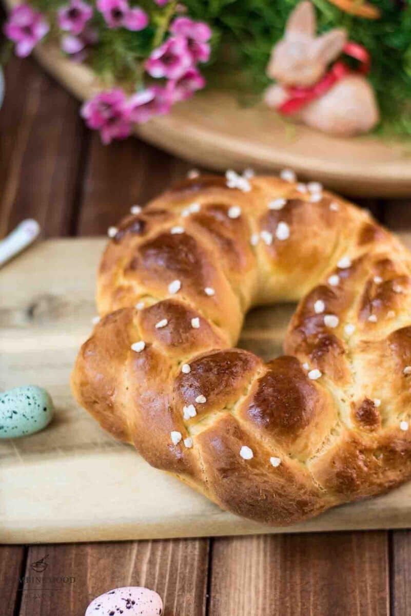 Gorgeous braided Easter bread wreath, placed on wooden cutting board, next to easter decoration.