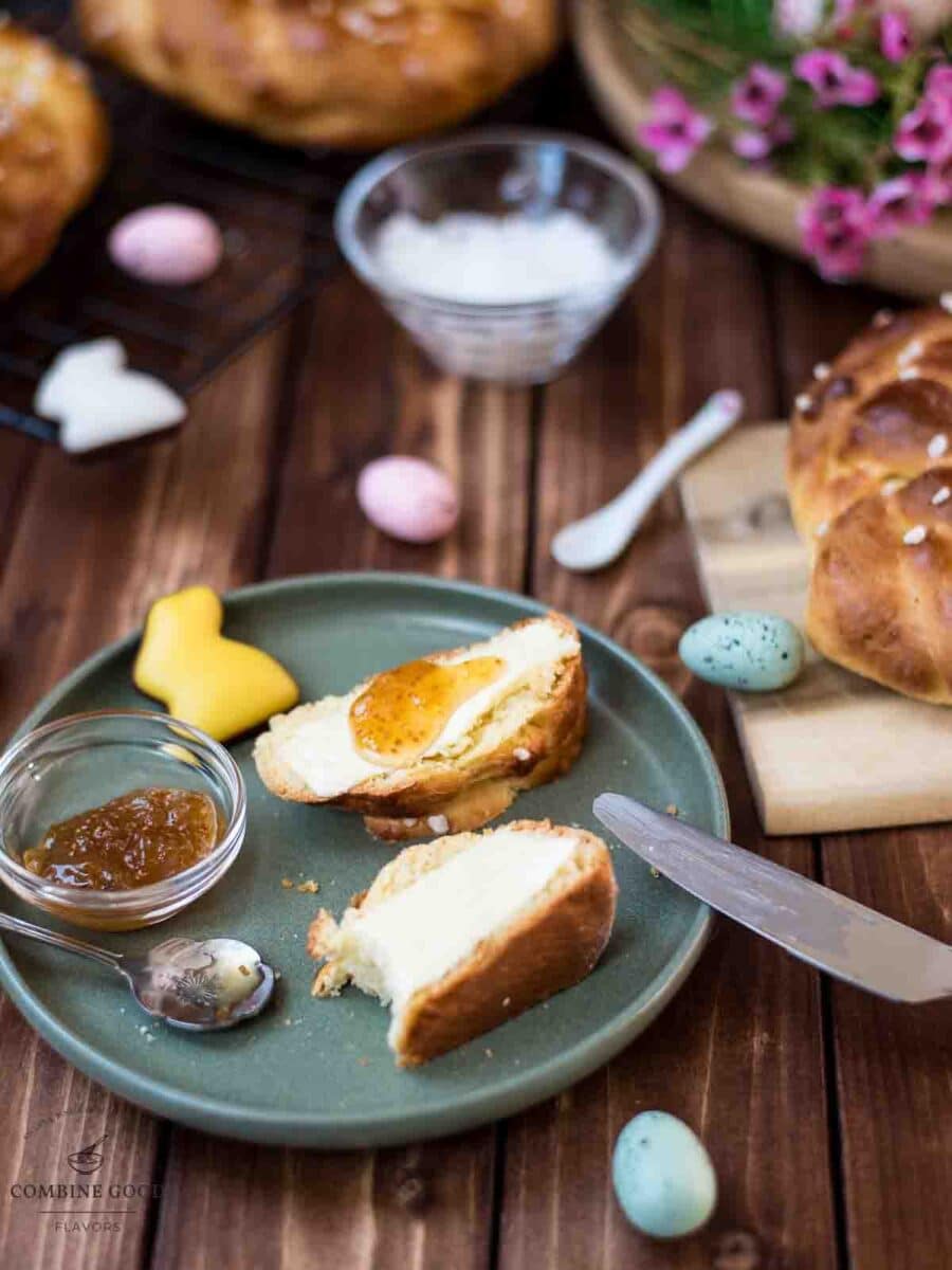 Sliced braided Easter bread wreath with butter and jam placed on green plate, next to Easter decoration.