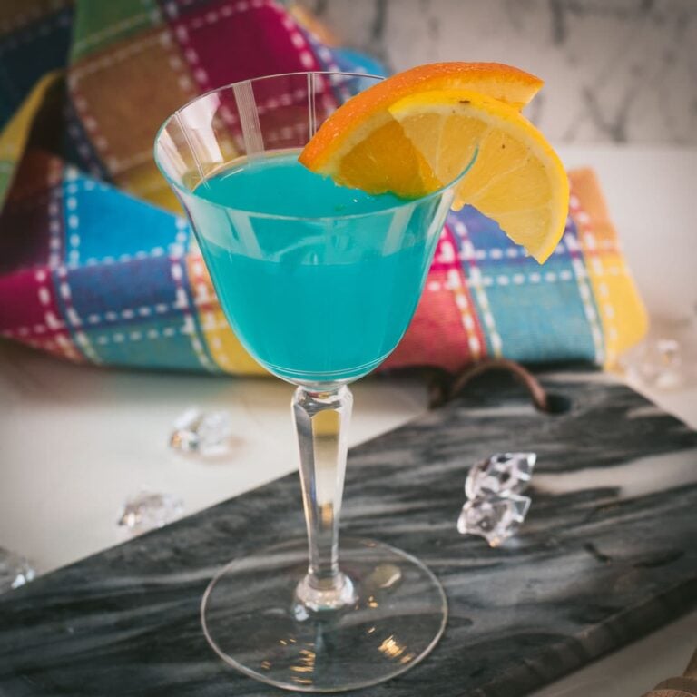 Gorgeous blue lady cocktail, served in vintage glass, garnished with an orange and an lemon slice side by side. Placed on a marbled plate.