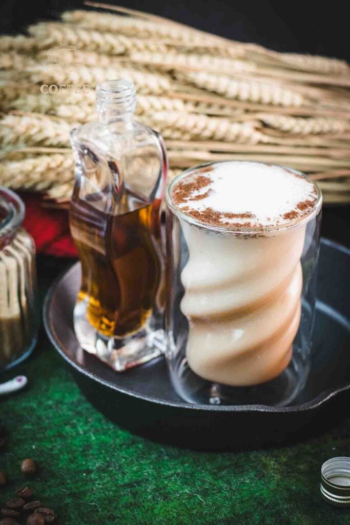 Curved glass filled with delicious brown sugar cinnamon latte, placed in a cast iron pan on a green felt base.