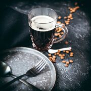Does Coffee Break a Fast? Glass filled with black coffee next to a dark plate with crossed spoon and fork.