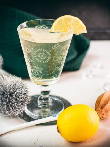 Glass with beautiful flower engraving, filled with delicious White Vermouth Blondie cocktail. Garnished with a lemon wedge.