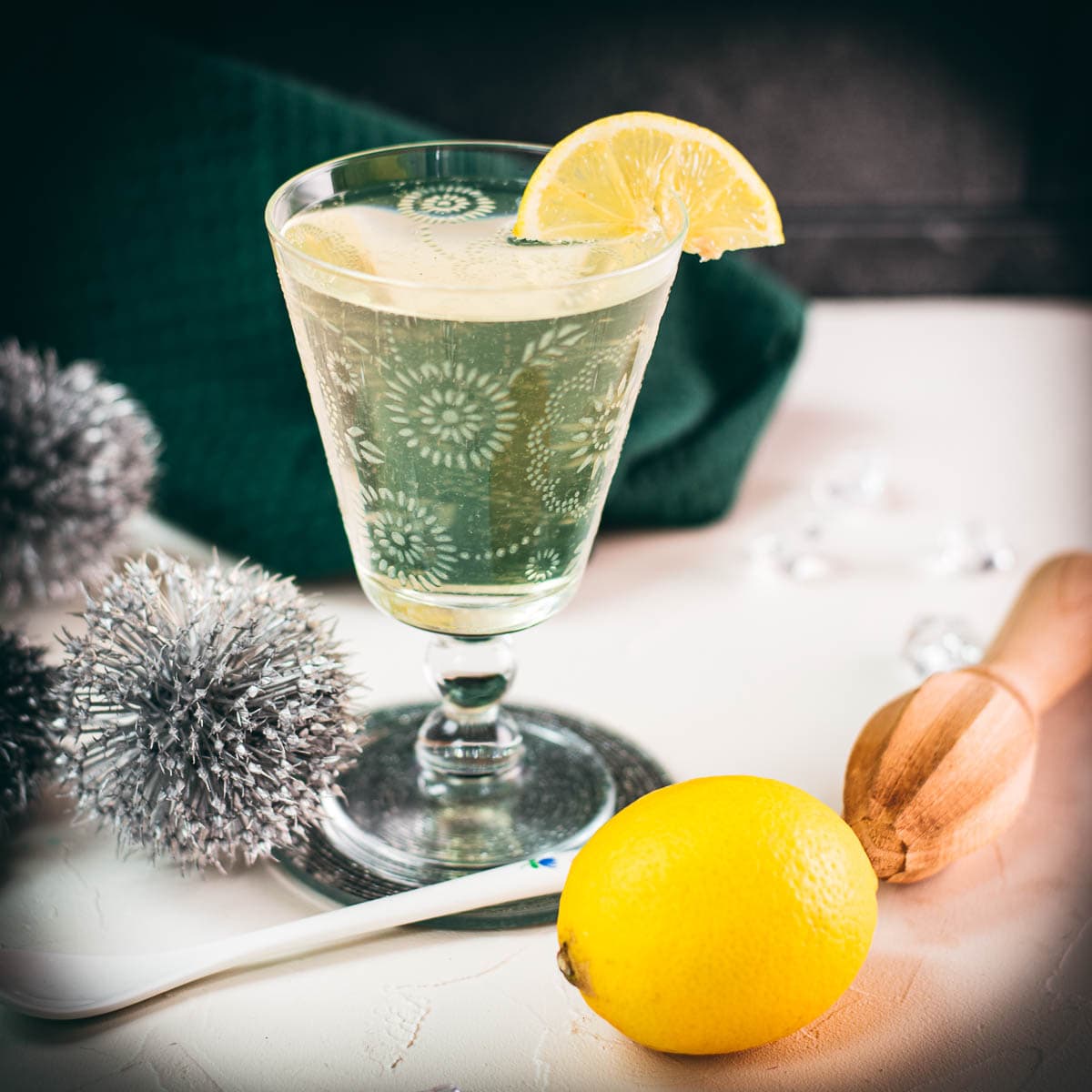 Glass with beautiful flower engraving, filled with delicious White Vermouth Blondie cocktail. Garnished with a lemon wedge.
