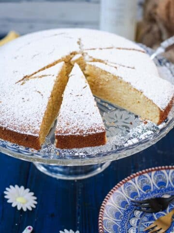 Delicious limoncello ricotta cake, sliced, on a glass cake stand.