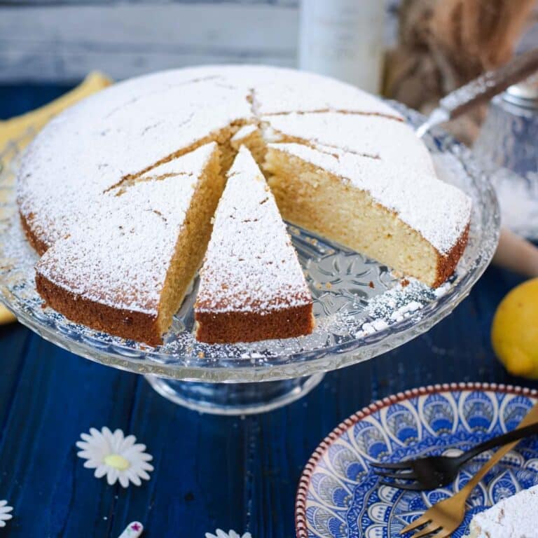 Delicious limoncello ricotta cake, sliced, on a glass cake stand.